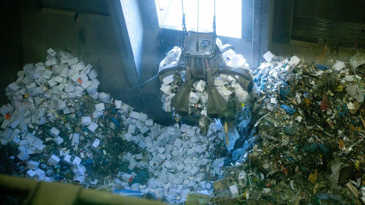 Eine Greifzange greift in einen großen Haufen Verpackungen in einer Müllanlage Eine Greifzange greift in einen großen Haufen Verpackungen in einer Müllanlage