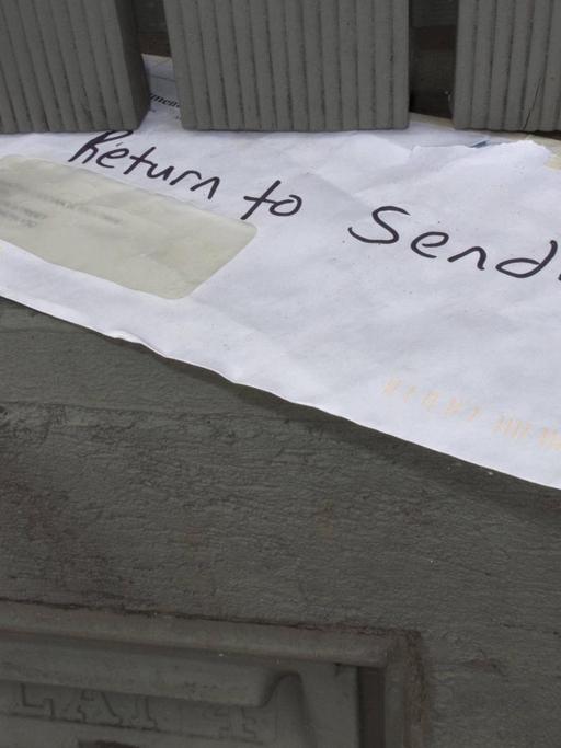 Ein weisser Briefumschlag steckt in einer Tür: "Return to sender" steht darauf.