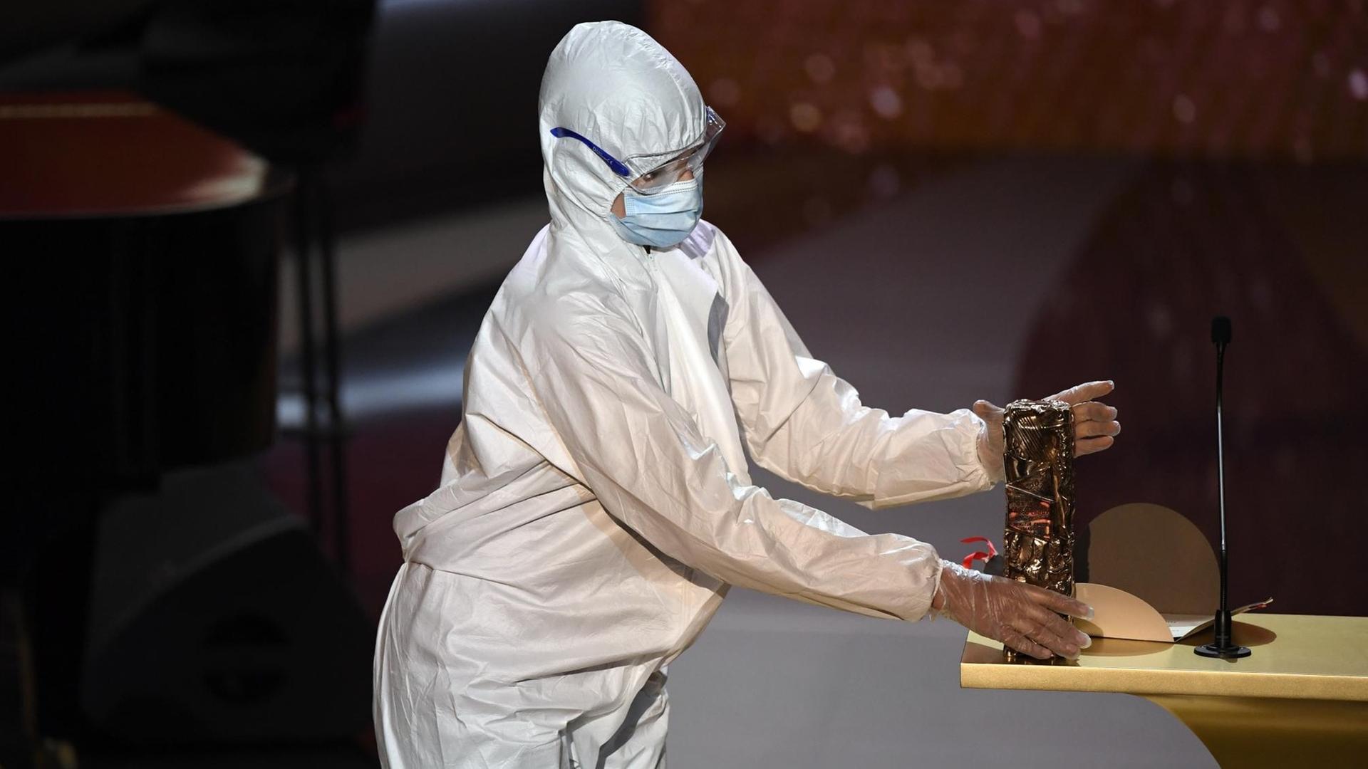Eine Person im Schutzanzug bringt eine César-Statue auf die Bühne Eine Person im Schutzanzug bringt eine César-Statue auf die Bühne