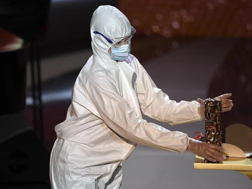 Eine Person im Schutzanzug bringt eine César-Statue auf die Bühne