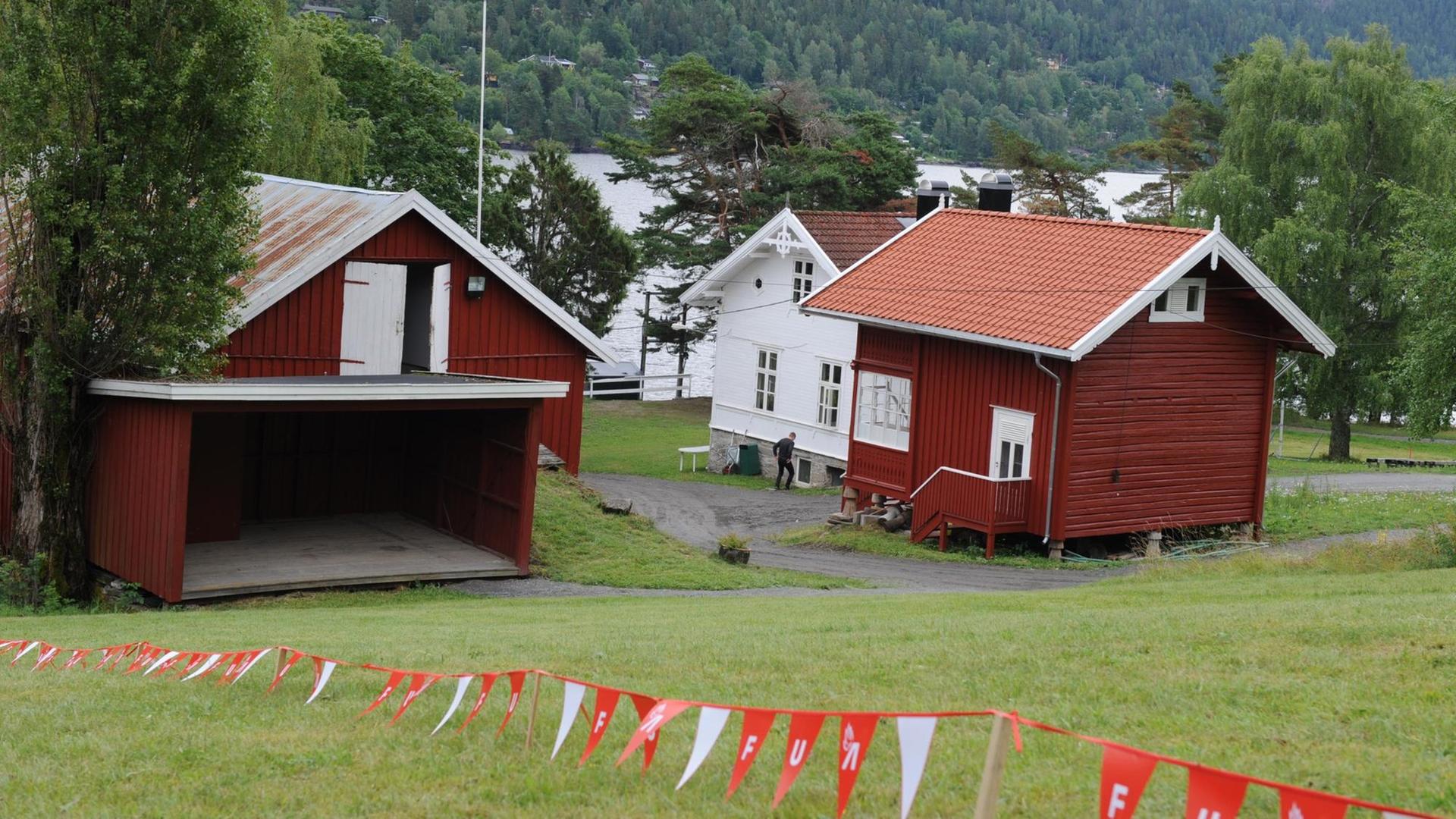 Drei Gebäude auf der norwegischen Insel Utøya. Im Vordergrund flattert ein rot-weißes Absperrband mit den Buchstaben AUF. Sie stehen für die Jugendorganisation der norwegischen Arbeiterpartei. Im Hintergrund sind Wasser und Bäume zu sehen. Drei Gebäude auf der norwegischen Insel Utøya. Im Vordergrund flattert ein rot-weißes Absperrband mit den Buchstaben AUF. Sie stehen für die Jugendorganisation der norwegischen Arbeiterpartei. Im Hintergrund sind Wasser und Bäume zu sehen.