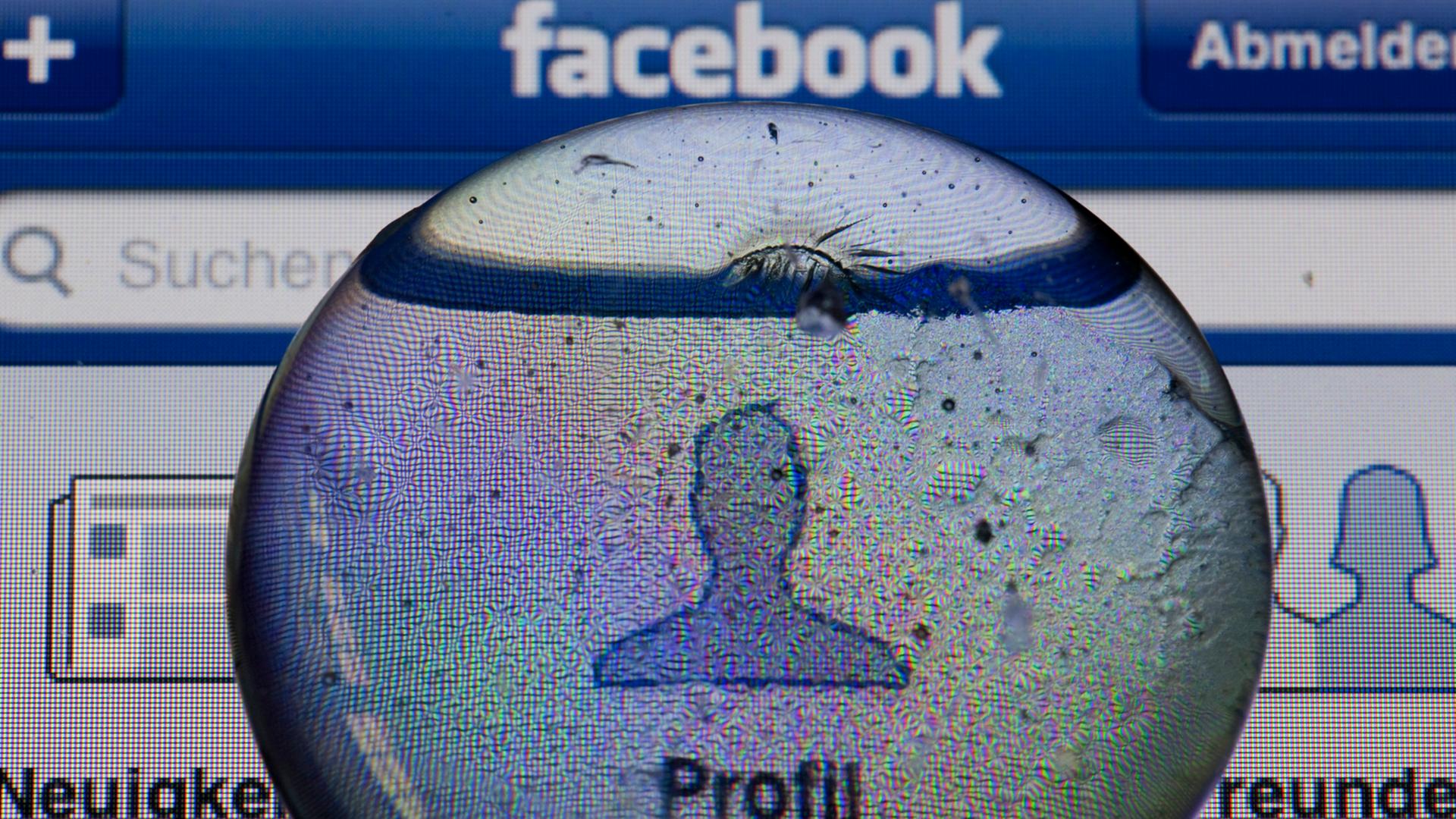 Ein Glasstein liegt auf dem Bildschirm eines iPhones und vergrößert das Profil-Icon einer Facebook-Anwendung. Ein Glasstein liegt auf dem Bildschirm eines iPhones und vergrößert das Profil-Icon einer Facebook-Anwendung.