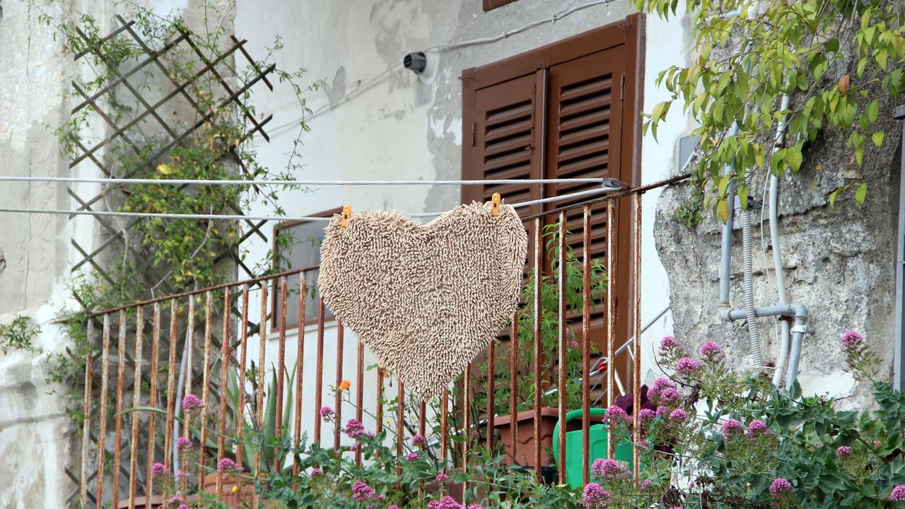 Eine herzförmige Fußmatte hängt an einer Wäscheleine vor dem Balkon eines Hauses in Matera Eine herzförmige Fußmatte hängt an einer Wäscheleine vor dem Balkon eines Hauses in Matera