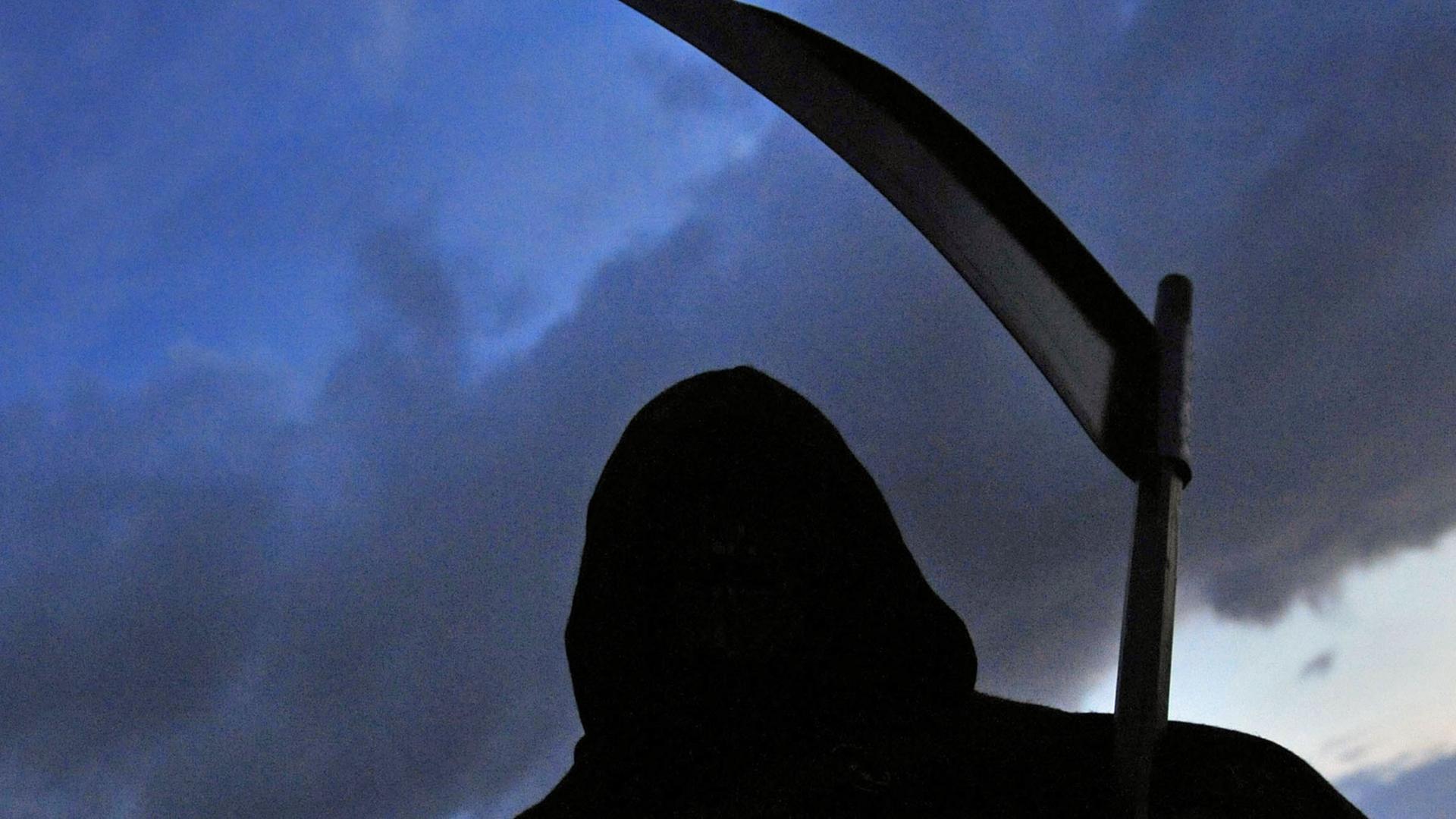 Die schwarze Silhoutte eines Sensenmanns mit Kapuze vor einem Himmel in der Dämmerung. Die schwarze Silhoutte eines Sensenmanns mit Kapuze vor einem Himmel in der Dämmerung.