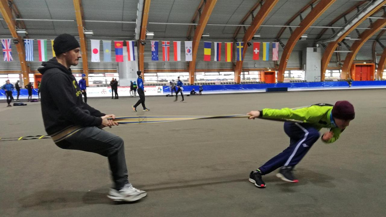 Ein gespanntes Seil zwischen Trainer und einem Nachwuchs-Eisschnellläufer in der richtigen Körperposition unter Spannung zu halten, ist Teil der Trockenübung