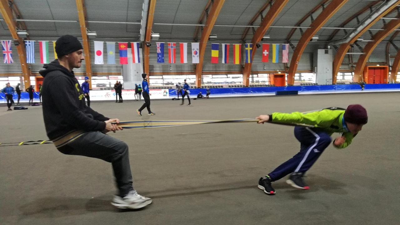 Ein gespanntes Seil zwischen Trainer und einem Nachwuchs-Eisschnellläufer in der richtigen Körperposition unter Spannung zu halten, ist Teil der Trockenübung Ein gespanntes Seil zwischen Trainer und einem Nachwuchs-Eisschnellläufer in der richtigen Körperposition unter Spannung zu halten, ist Teil der Trockenübung