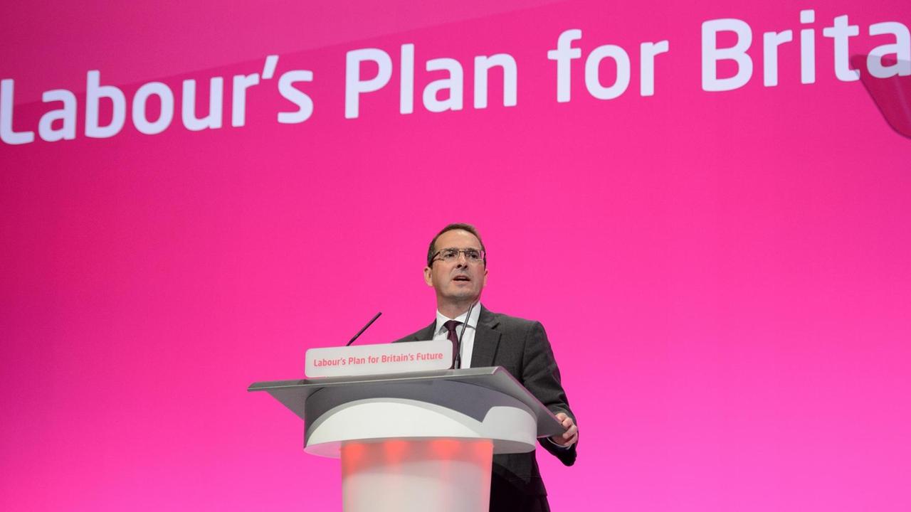 Smith spricht am Rednerpult vor einem magentafarbenen Hintergrund mit dem Schriftzug "Labour's Plan for Britain".