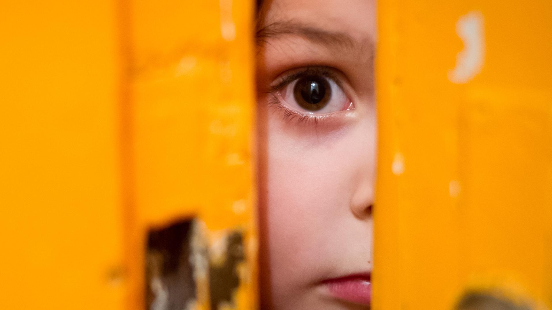 Ein junges Mädchen schaut durch einen Türschlitz.