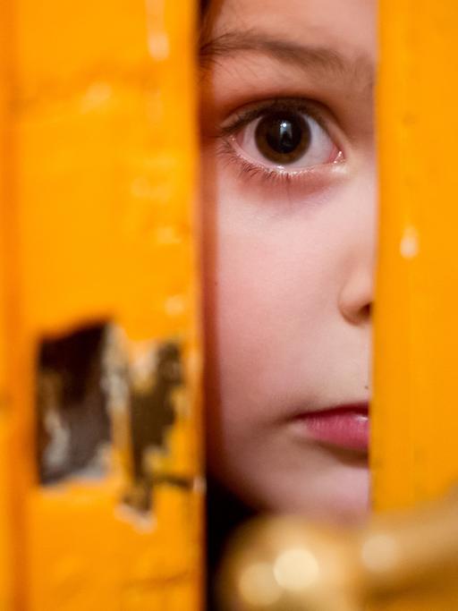 Ein junges Mädchen schaut durch einen Türschlitz.