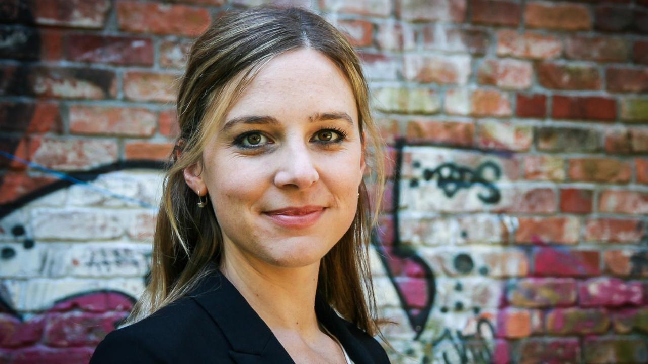 Pfarrerin Corinna Zisselsberger steht vor einer roten, mit Graffiti besprühten Backsteinwand und schaut freundlich in die Kamera. Pfarrerin Corinna Zisselsberger steht vor einer roten, mit Graffiti besprühten Backsteinwand und schaut freundlich in die Kamera.