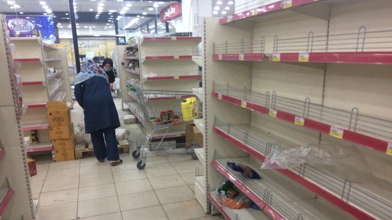 Zwei Menschen gehen durch einen Supermarkt mit nahezu leer gekauften Regalen Zwei Menschen gehen durch einen Supermarkt mit nahezu leer gekauften Regalen