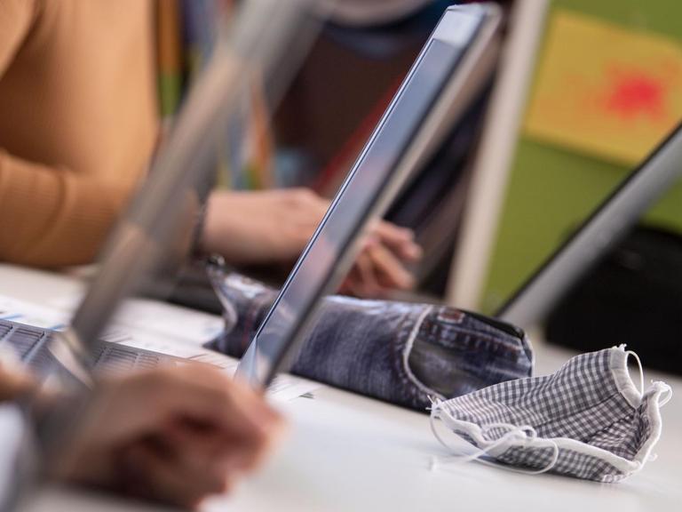 Mehrere Laptops stehen nebeneinander auf dem Tisch eines Klassenzimmers. 
