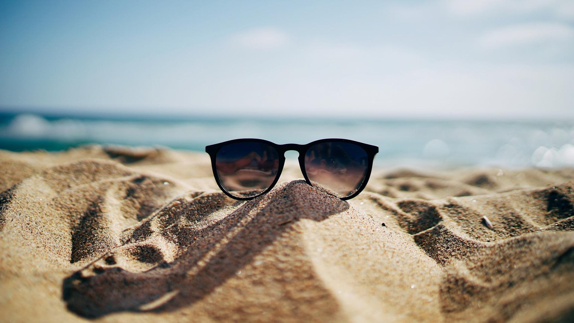 Eine Sonnenbrille liegt im Sand an einem Strand.