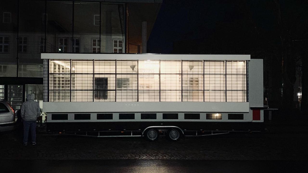 Abbildung eines dem Bauhausgebäude nachempfundenen Tiny Houses auf einem Anhänger. Abbildung eines dem Bauhausgebäude nachempfundenen Tiny Houses auf einem Anhänger.