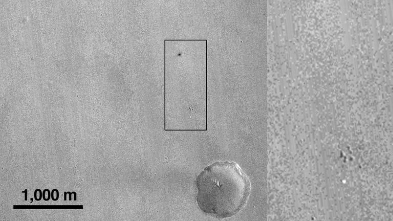 Von der NASA-Sonde Mars Reconnaissance Orbiter aufgenommenes Bild der Mars-Oberfläche vom 21. Oktober 2016. Laut ESA könnte das hellere Objekt am unteren Rand des Bildes den Fallschirm und der obige dunkle Punkt den Einschlagskrater des Landers zeigen Von der NASA-Sonde Mars Reconnaissance Orbiter aufgenommenes Bild der Mars-Oberfläche vom 21. Oktober 2016. Laut ESA könnte das hellere Objekt am unteren Rand des Bildes den Fallschirm und der obige dunkle Punkt den Einschlagskrater des Landers zeigen