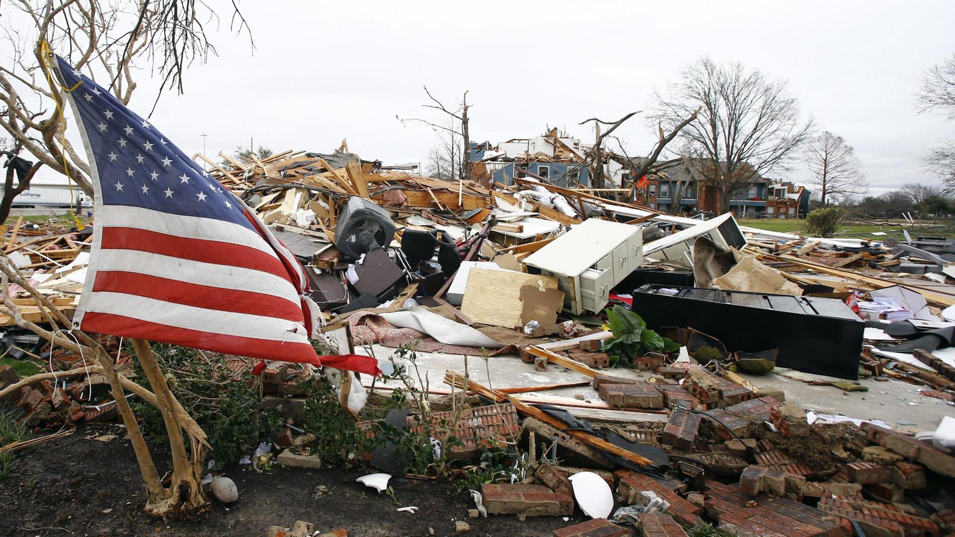 Die amerikanische Flagge vor den Trümmern eines Hauses, das von einem Tornado zerstört wurde. Die amerikanische Flagge vor den Trümmern eines Hauses, das von einem Tornado zerstört wurde.