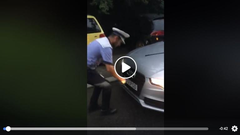 Ein Polizist kniet in einem Handyvideo, um das Nummernschild eines Autos abzunehmen.