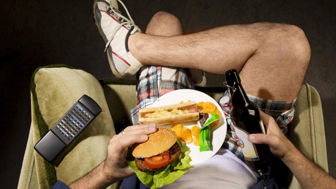 Ein Mann sitzt auf der Couch, ist Junk Food und trinkt Bier. Ein Mann sitzt auf der Couch, ist Junk Food und trinkt Bier.