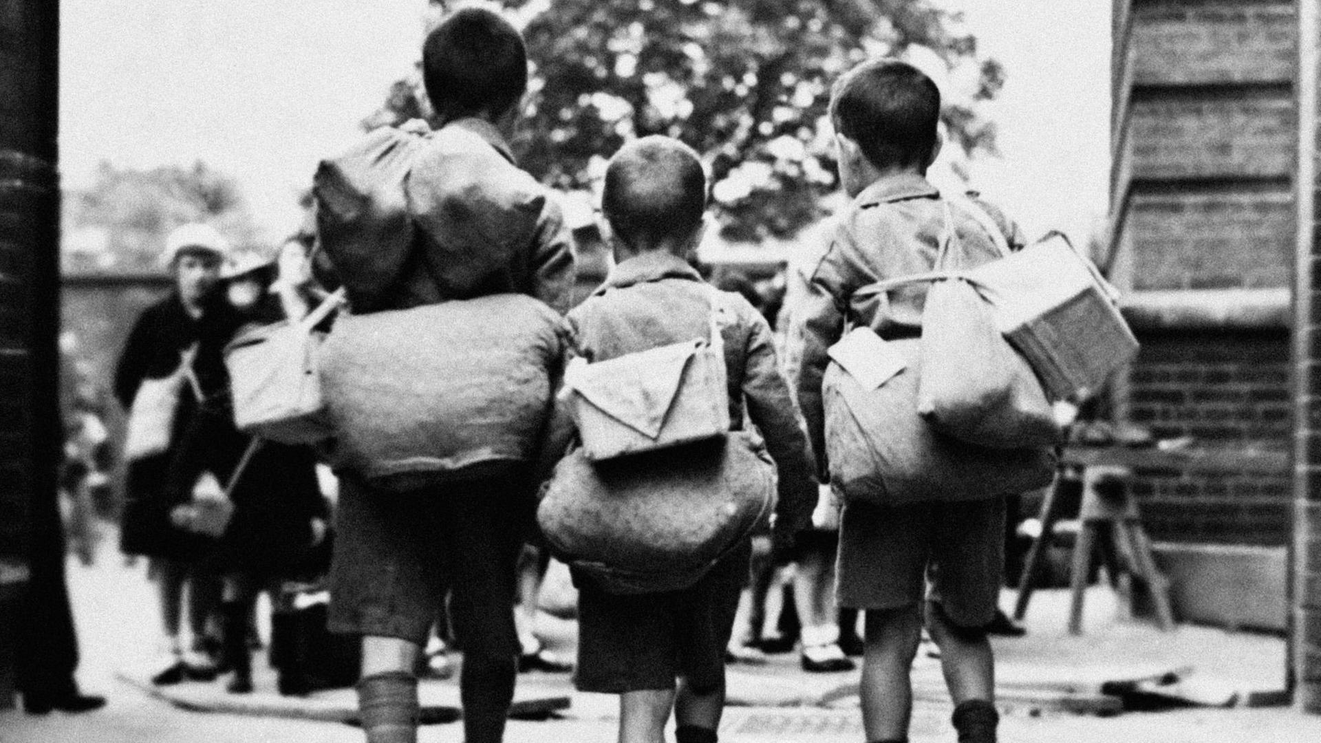 Kinderverschickung: undatierte historische Aufnahme von drei Kindern mit Gepäck auf dem Rücken. Kinderverschickung: undatierte historische Aufnahme von drei Kindern mit Gepäck auf dem Rücken.