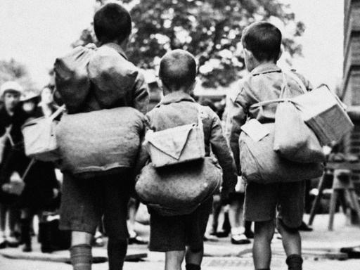 Kinderverschickung: undatierte historische Aufnahme von drei Kindern mit Gepäck auf dem Rücken.