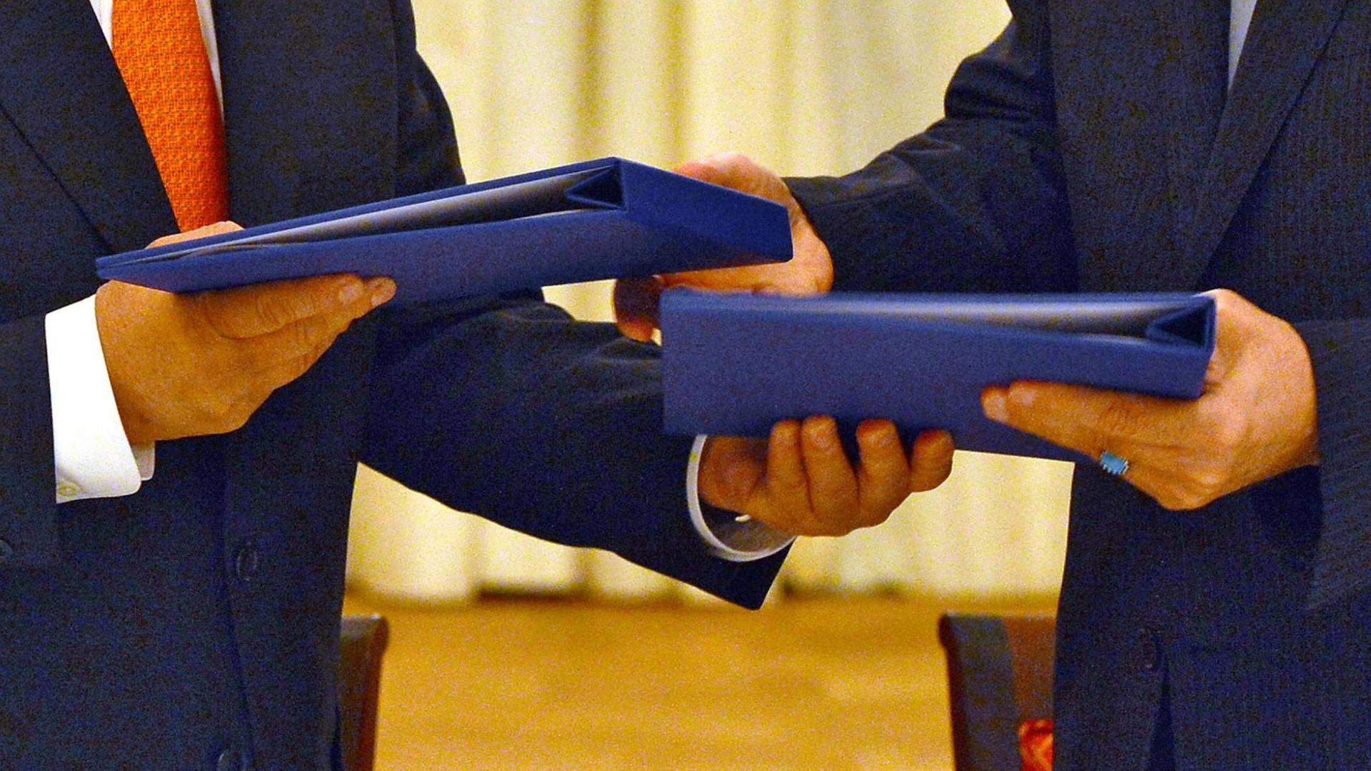 Zu sehen sind zwei blaue Mappen, die linke hält der Chef der internationalen Atomenergiebehörde, Amano, die rechte der iranische Chefunterhändler Salehi Zu sehen sind zwei blaue Mappen, die linke hält der Chef der internationalen Atomenergiebehörde, Amano, die rechte der iranische Chefunterhändler Salehi