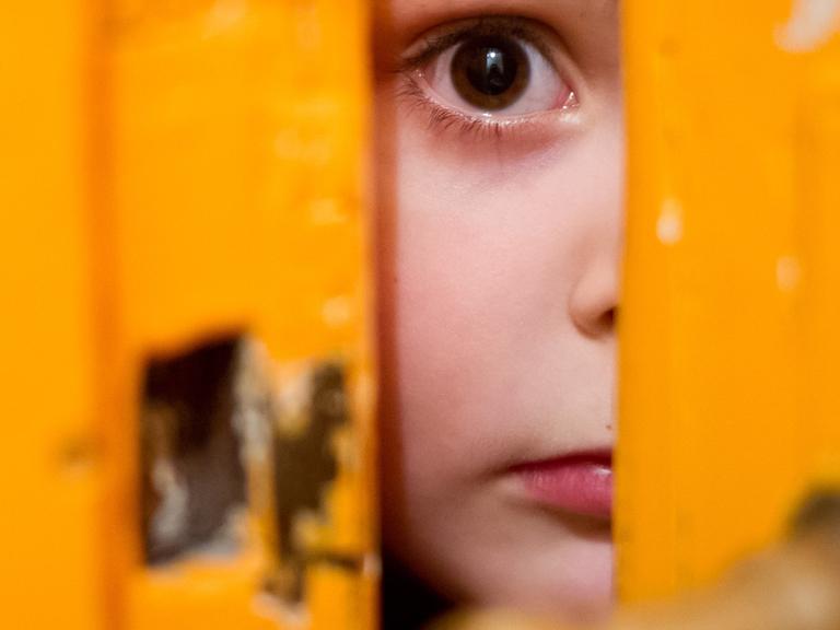 Ein junges Mädchen schaut am 24.01.2014 in Berlin durch einen Türschlitz.