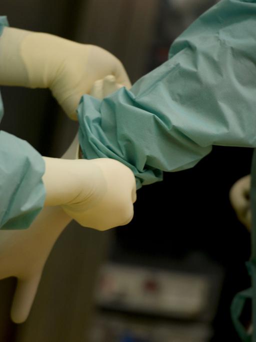 Ein Mediziner bekommt am 18.02.2014 in einer Klinik in Baden-Württemberg vor einer Operation ein Paar Handschuhe angezogen.