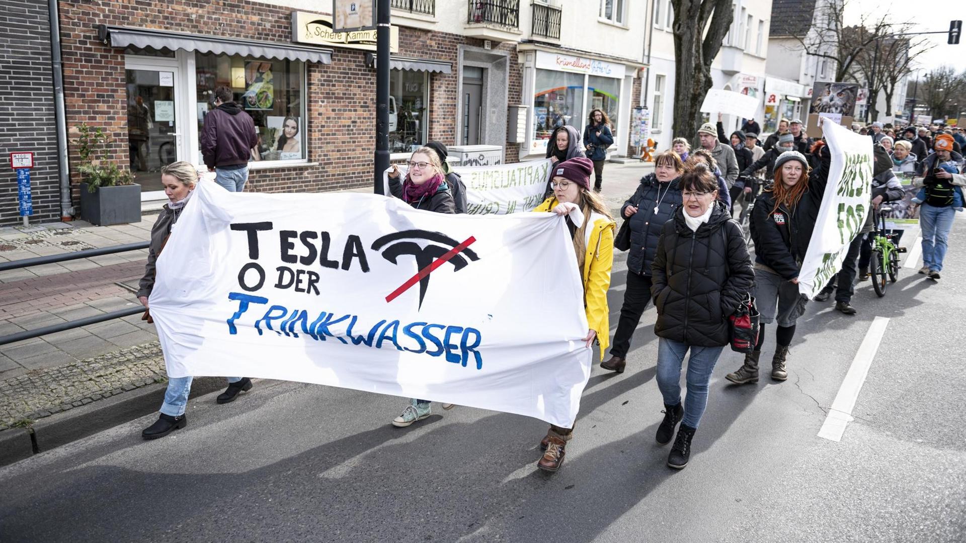 Demonstranten halten auf einer Demo gegen die geplante Tesla-Fabrik in Grünheide ein Banner mit der Aufschrift "Tesla oder Trinkwasser". Demonstranten halten auf einer Demo gegen die geplante Tesla-Fabrik in Grünheide ein Banner mit der Aufschrift "Tesla oder Trinkwasser".