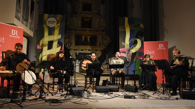 Unter einer Kirchenorgel sitzen Musiker auf einer Bühne.