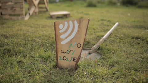 Auf einem Holzbrett steht „No Wifi Zon“ — dahinter liegt ein Spaten.