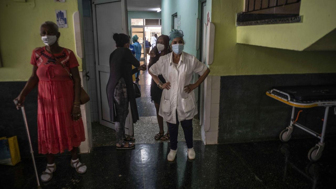 Medizinisches Personal und andere Menschen stehen auf einem Gang in einem Gebäude in Havanna.
