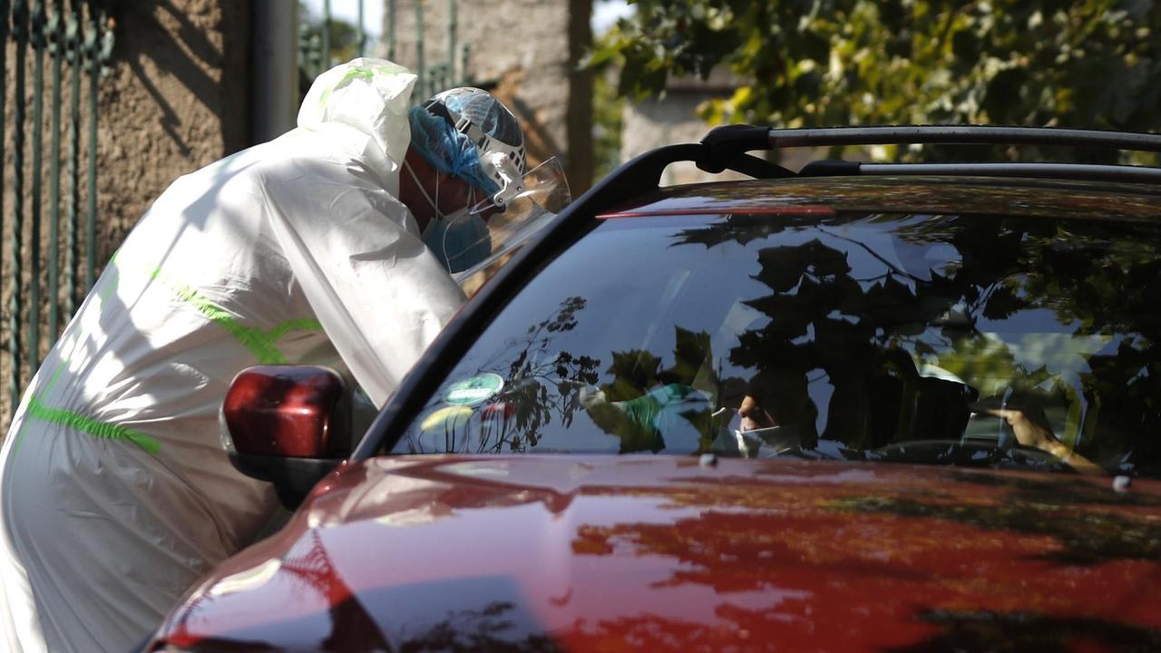 Ein medizinischer Mitarbeiter in Schutzausrüstung untersucht einen jungen Autofahrer an einer Drive-in-Teststation auf Covid-19-Symptome. Ein medizinischer Mitarbeiter in Schutzausrüstung untersucht einen jungen Autofahrer an einer Drive-in-Teststation auf Covid-19-Symptome.