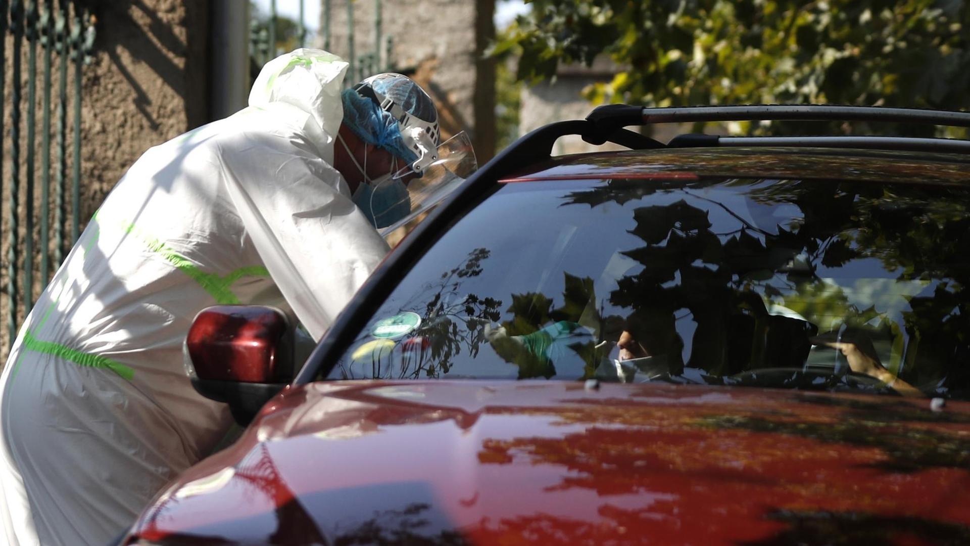 Ein medizinischer Mitarbeiter in Schutzausrüstung untersucht einen jungen Autofahrer an einer Drive-in-Teststation auf Covid-19-Symptome.