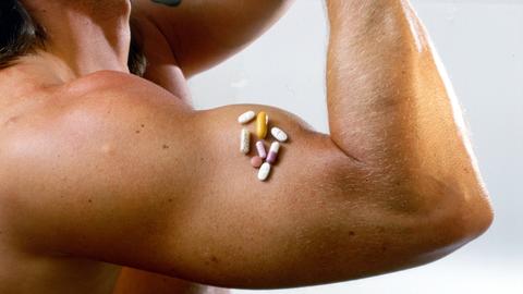 Anabolika-Missbrauch: mit Pillen schnell zum Traumkörper. Auf dem muskulösen Oberarm eines Bodybuilders liegen verschiedene Anabolika-Präparate.