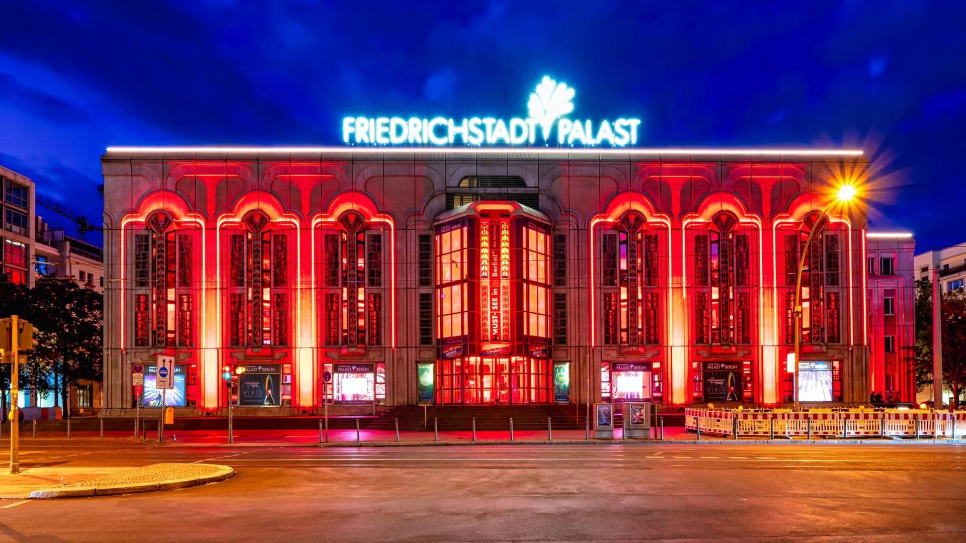 Der Friedrichstadt-Palast in verschiedenen Farben angestrahlt, vor nachtblauem Himmel. 