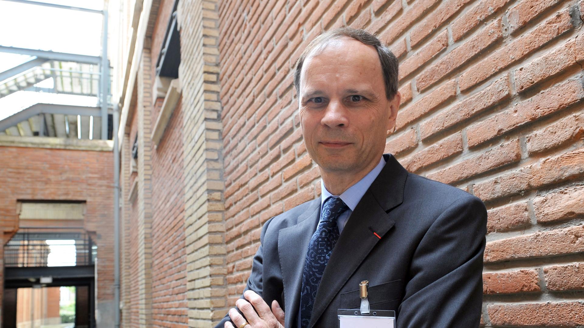 Jean Tirole steht, die Arme verschränkt, vor einer Mauer. Jean Tirole steht, die Arme verschränkt, vor einer Mauer.
