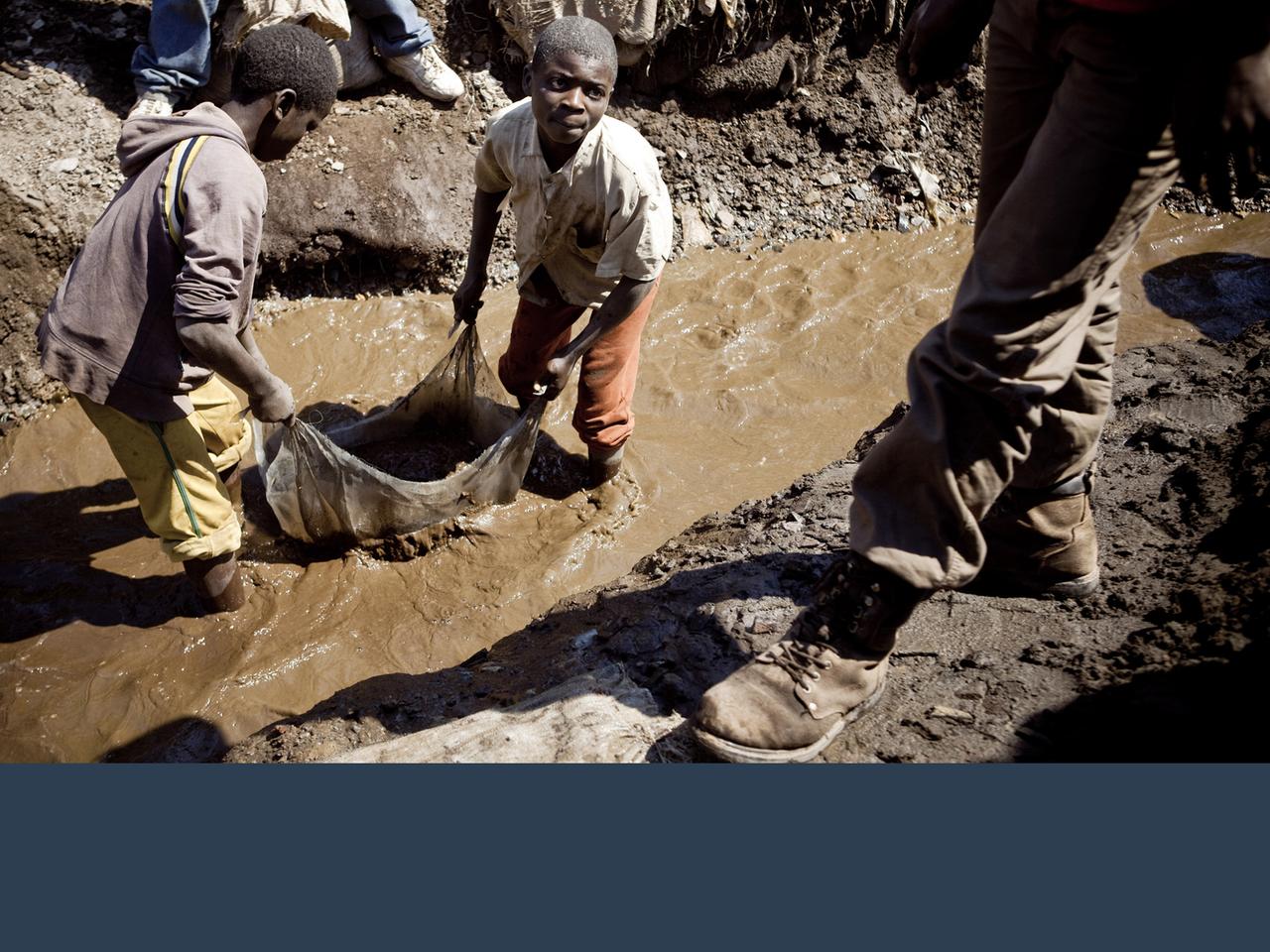 Zu sehen sind Kinder, die in einer Kupfermine arbeiten. Sie stehen bis zu den Knien im Schlamm. 