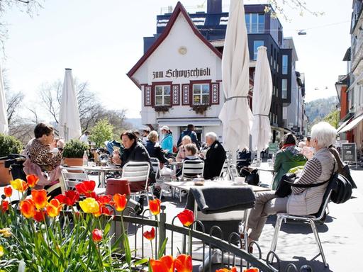 Bei frühlingshaftem Wetter sitzen Gäste in der idylischen schweizer Kleinstadt Baden draußen an Tischen vor einem Restaurant namens "Zum Schwyzerhüsli".