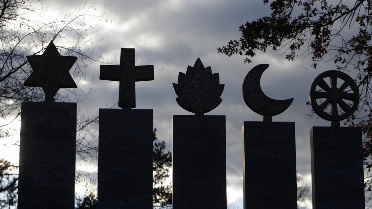 Fuenf Symbole aus Stein fuer die Weltreligionen Judentum, Christentum, Hinduismus, Islam und Buddhismus stehen im Gegenlicht Fuenf Symbole aus Stein fuer die Weltreligionen Judentum, Christentum, Hinduismus, Islam und Buddhismus stehen im Gegenlicht