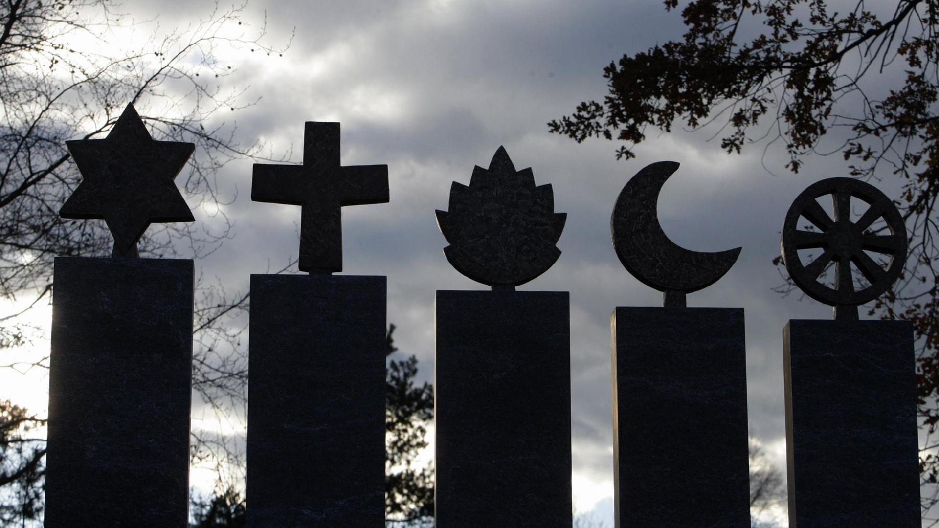 Fuenf Symbole aus Stein fuer die Weltreligionen Judentum, Christentum, Hinduismus, Islam und Buddhismus stehen im Gegenlicht Fuenf Symbole aus Stein fuer die Weltreligionen Judentum, Christentum, Hinduismus, Islam und Buddhismus stehen im Gegenlicht