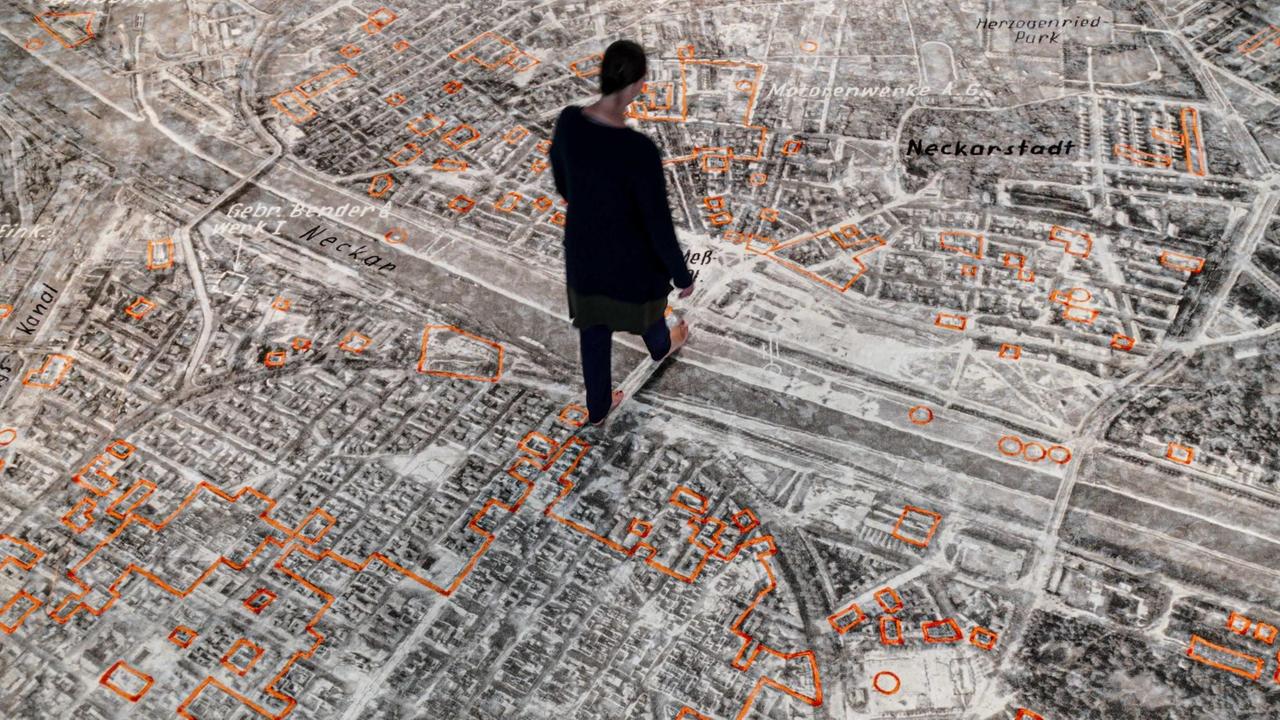Eine Person läuft über eine auf einen Teppich applizierte Bodengrafik, die die zerbombte Stadt Mannheim von oben zeigt. Eine Person läuft über eine auf einen Teppich applizierte Bodengrafik, die die zerbombte Stadt Mannheim von oben zeigt.