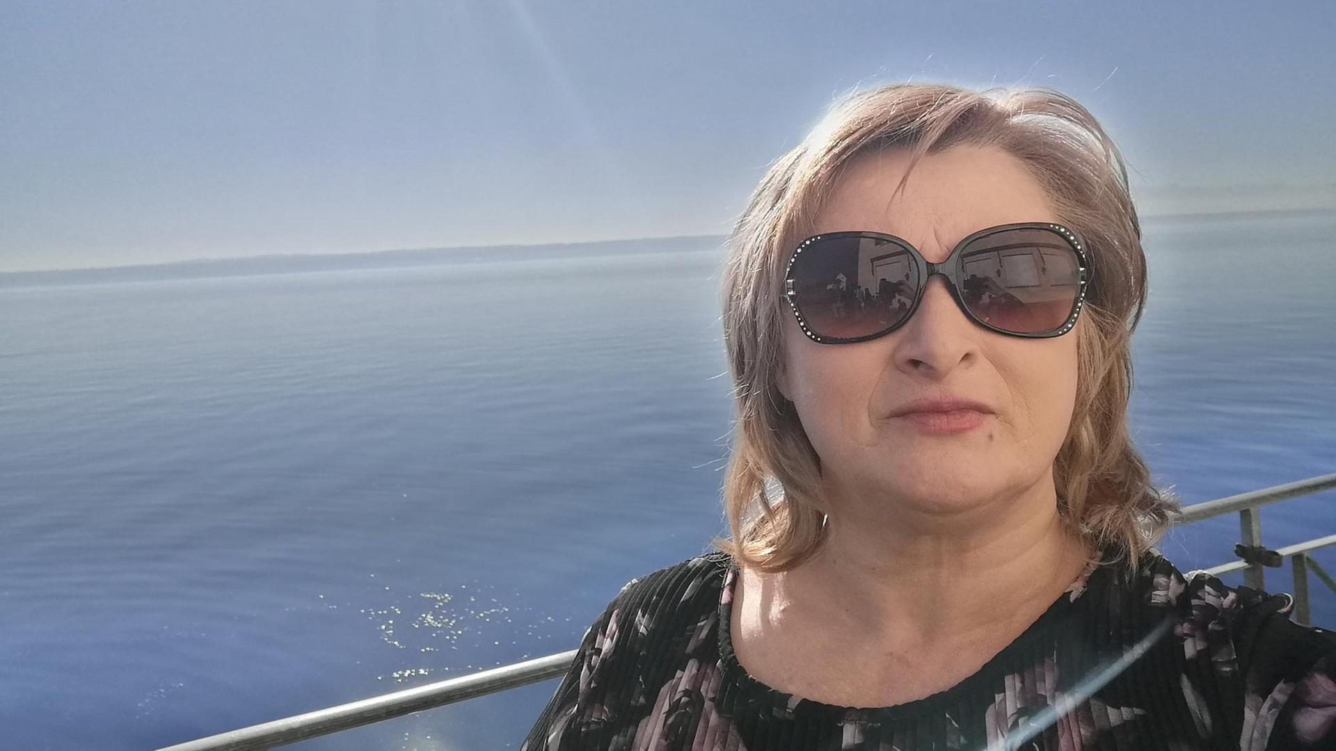 Eine Frau mit Sonnenbrille. Im Hintergrund ist das Wasser eines großen Sees zu sehen. Eine Frau mit Sonnenbrille. Im Hintergrund ist das Wasser eines großen Sees zu sehen.