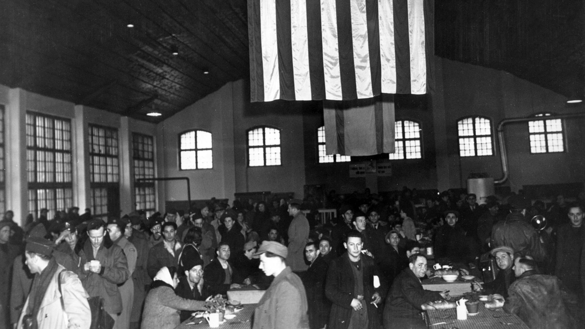 Eine große amerikanische Flagge hängt in der Halle des DP Camps Landsberg, in der die Mahlzeiten eingenommen werden, von der Decke. In der Saarburgkaserne in Landsberg am Lech wurde nach der Besetzung der Stadt durch US-Truppen von der Nothilfe- und Wiederaufbauverwaltung der Vereinten Nationen (United Nations Relief and Rehabilitation Administration, kurz UNRRA) ein Lager für verschleppte Juden eingerichtet. Aufnahme vom 6.12.1945 Eine große amerikanische Flagge hängt in der Halle des DP Camps Landsberg, in der die Mahlzeiten eingenommen werden, von der Decke. In der Saarburgkaserne in Landsberg am Lech wurde nach der Besetzung der Stadt durch US-Truppen von der Nothilfe- und Wiederaufbauverwaltung der Vereinten Nationen (United Nations Relief and Rehabilitation Administration, kurz UNRRA) ein Lager für verschleppte Juden eingerichtet. Aufnahme vom 6.12.1945