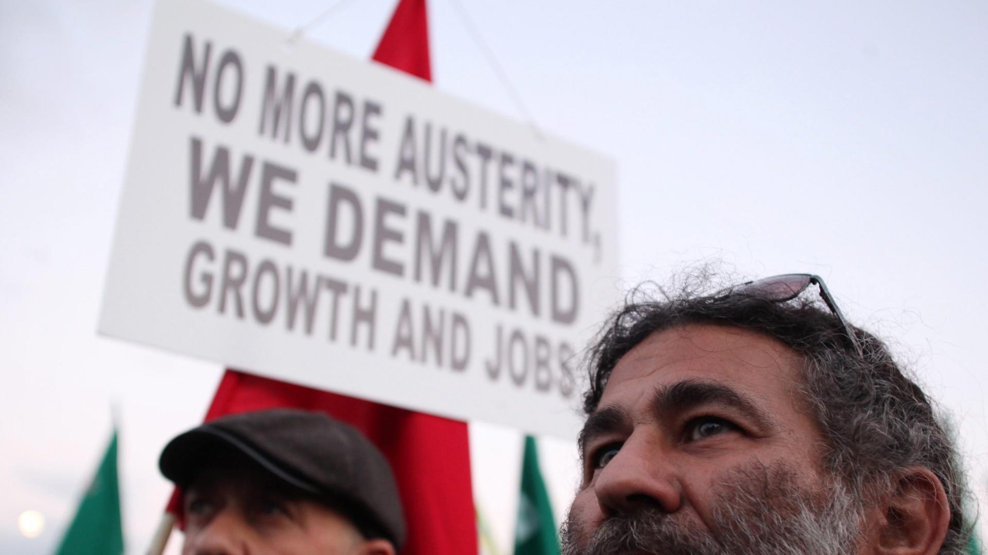Zwei Demonstranten, im Hintergrund ein Plakat mit der Aufschrift: "No more austerity, we demand jobs and growth"