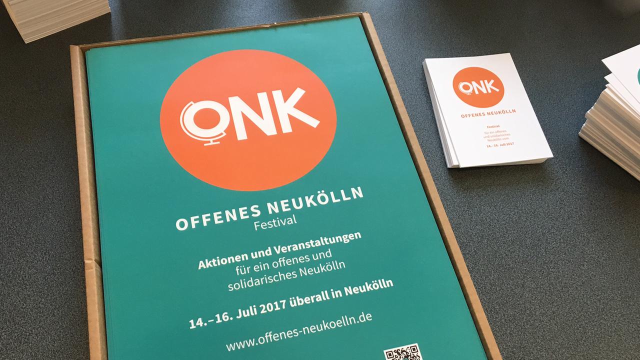 Plakate für das Offenes Neukölln Festival vom 14. bis 16. Juli 2017 liegen gestapelt mit Flyern auf einem Tisch. 