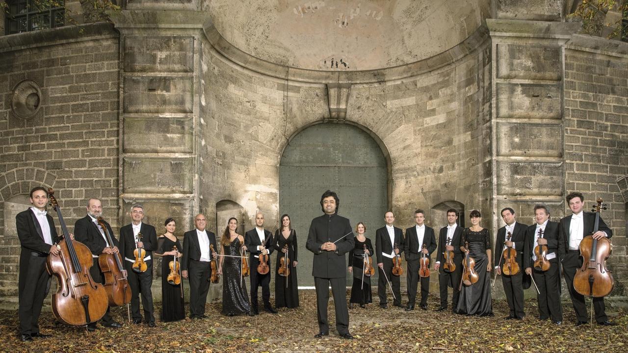 Das Orchester steht mit seinem Chefdirigenten in einem historischen Basilikagemäuer. Das Orchester steht mit seinem Chefdirigenten in einem historischen Basilikagemäuer.