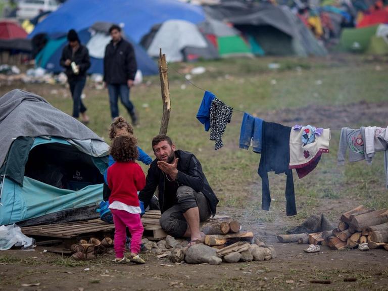 Ein Mann mit zwei Kindern sitzt am 11.03.2016 vor seinem Zelt im Flüchtlingslager in Idomeni an der Grenze zwischen Griechenland und Mazedonien.