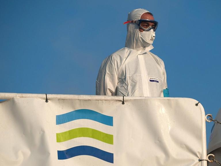 Ein Mann in Schutzkleidung steht am 25. Juli 2020 vor Malaga auf einem Schiff mit Frontex-Fahne