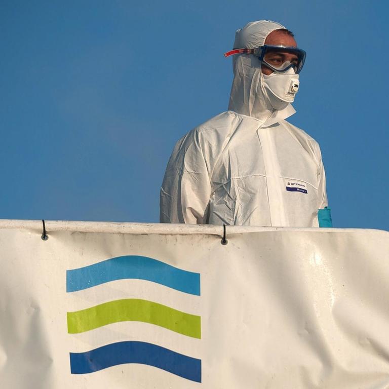 Ein Mann in Schutzkleidung steht am 25. Juli 2020 vor Malaga auf einem Schiff mit Frontex-Fahne 