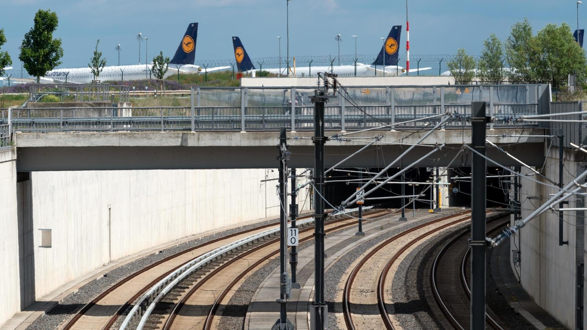 02.06.2020, Brandenburg, Potsdam: Die Schienen der S-Bahn (l) und der Regionalbahn führen in einen Tunnel zum unterírdischen Bahnhof des Hauptstadtflughafens. Im Hintergrund stehen abseits des Rollfeldes Flugzeuge der Fluggesellschaft Lufthansa. Foto: Soeren Stache/dpa-Zentralbild/ZB | Verwendung weltweit 02.06.2020, Brandenburg, Potsdam: Die Schienen der S-Bahn (l) und der Regionalbahn führen in einen Tunnel zum unterírdischen Bahnhof des Hauptstadtflughafens. Im Hintergrund stehen abseits des Rollfeldes Flugzeuge der Fluggesellschaft Lufthansa. Foto: Soeren Stache/dpa-Zentralbild/ZB | Verwendung weltweit